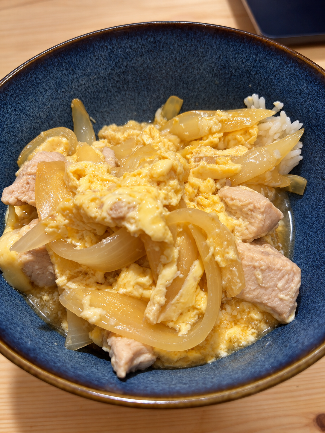 A bowl of oyakodon with tender chicken, softly set egg, onion, and sliced green onion